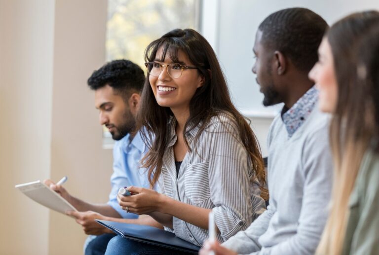Four employees sitting down in a meeting taking notes.